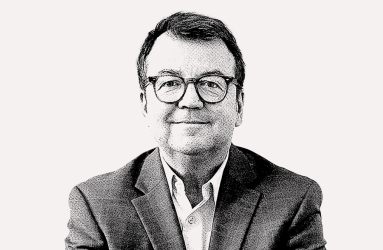 Schwarz-weiß Portrait eines Mannes mit Brille im Anzug, auf hellem Hintergrund.