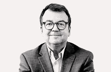 Schwarz-weiß Bild eines Mannes im Anzug mit Brille, neutraler Hintergrund.