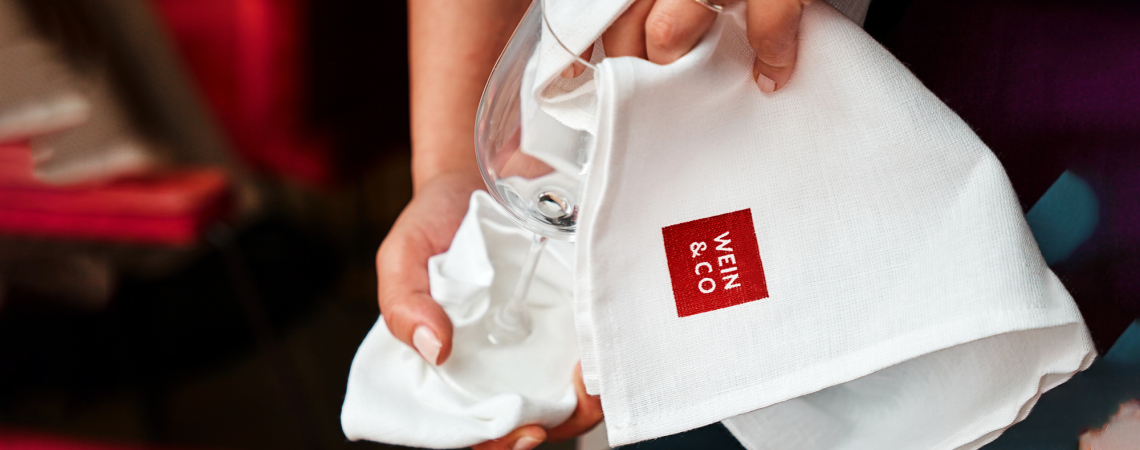 Hand poliert Weinglas mit weißem Tuch in eleganter Umgebung.