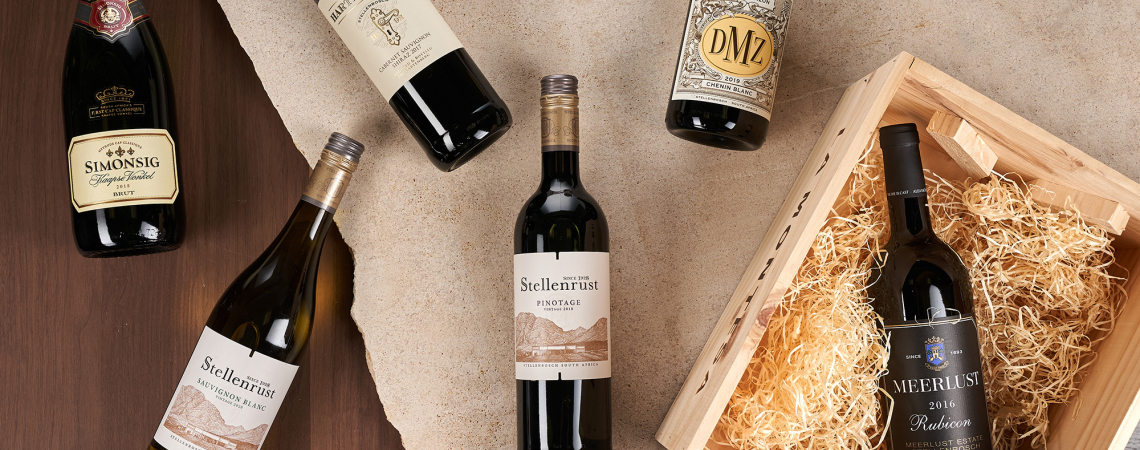 Verschiedene Weinflaschen stilvoll auf Holztisch und Jutestoff mit Holzbox arrangiert.