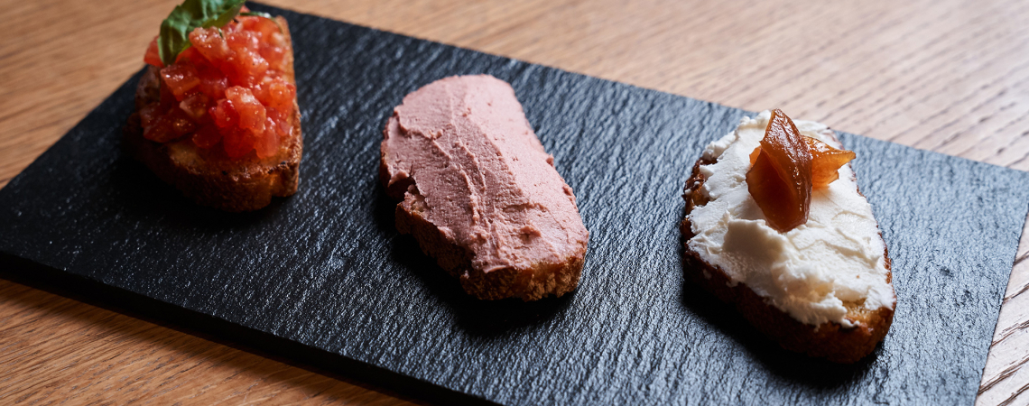 Drei belegte Crostini auf schwarzer Schieferplatte, appetitlich angerichtet.