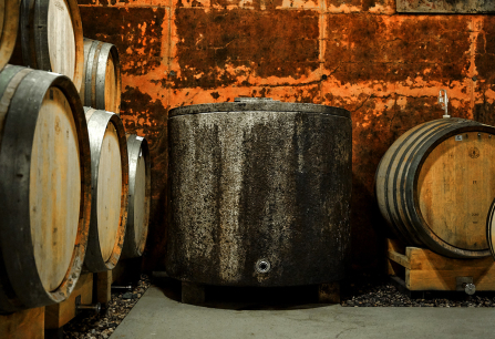 Weinfässer aus Holz und Metall in rustikalem Keller mit Backsteinwänden.