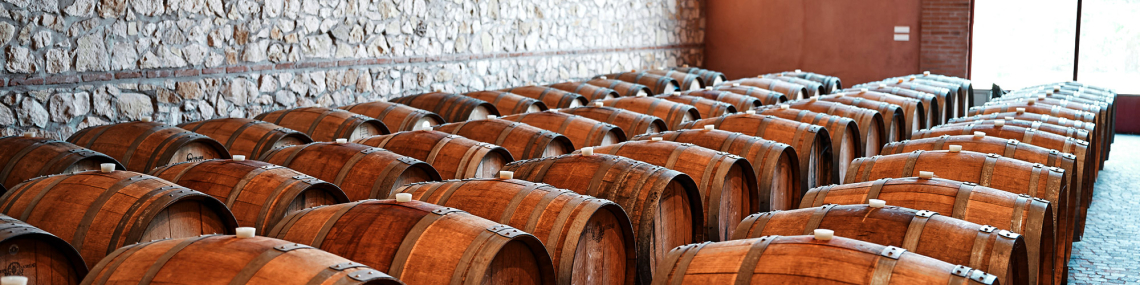 Holzfässer in Reihen in einem Weinkeller mit Steinmauer.
