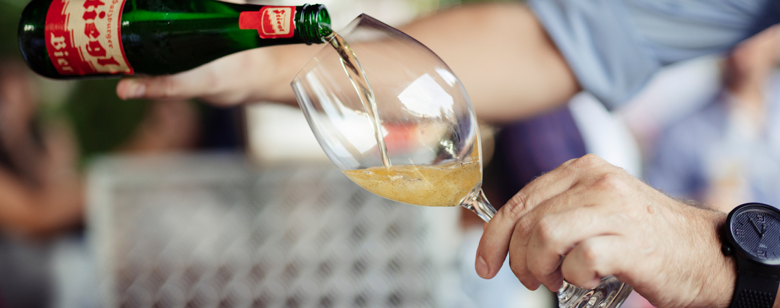 Grüne Flasche gießt goldenes Getränk in ein klares Weinglas.