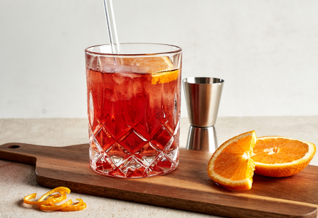 Roter Cocktail im Kristallglas auf Holzbrett mit Orangenscheiben.