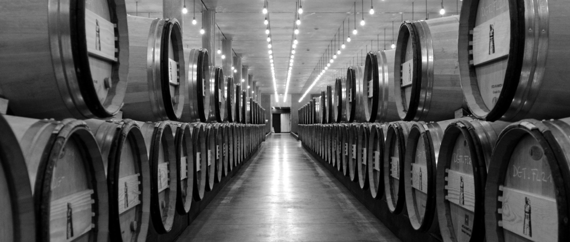 Schwarzweiß-Foto von einer langen Reihe großer Holzfässer in einem Weinkeller.
