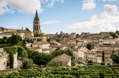 Historische Stadtlandschaft mit Kirche, Weinbergen und mittelalterlicher Architektur unter blauem Himmel.