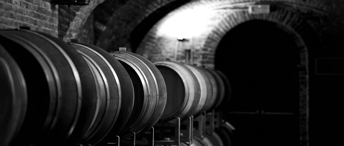 Schwarz-weiß Bild von hölzernen Weinfässern in einem traditionellen Kellergewölbe.