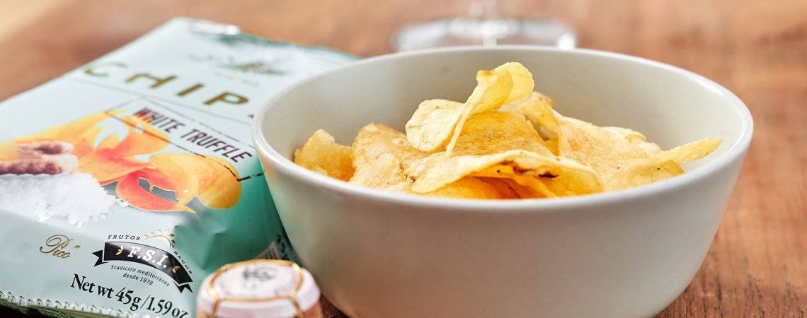 Schale mit knusprigen Chips neben einer Chipstüte auf Holztisch.