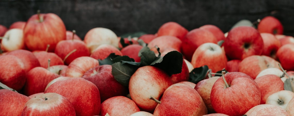 Frische, rote Äpfel in einer Holzkiste, umgeben von grünen Blättern.