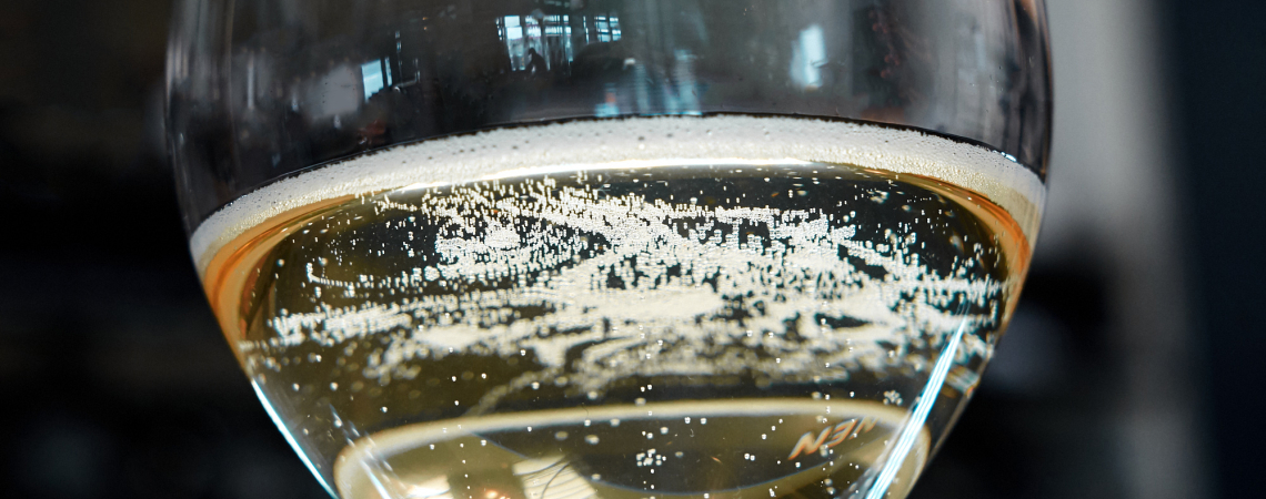 Nahaufnahme eines Champagnerglases mit sprudelndem Sekt vor unscharfem Hintergrund.