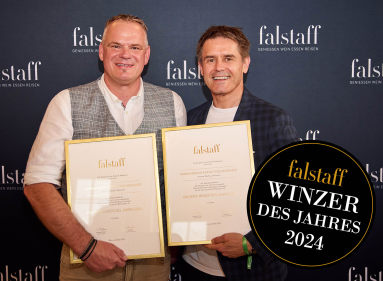 Zwei Männer mit Urkunden vor einem Falstaff-Hintergrund, runde schwarze Plakette rechts.