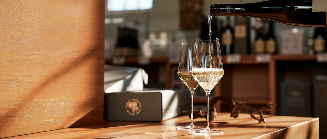 Zwei Weingläser mit Sekt in warmem Sonnenlicht auf Holztisch.