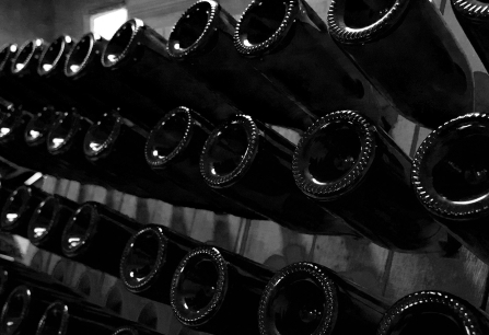 Schwarz-weiß Foto von aufgereihten, kopfüber gelagerten Weinflaschen im Keller.