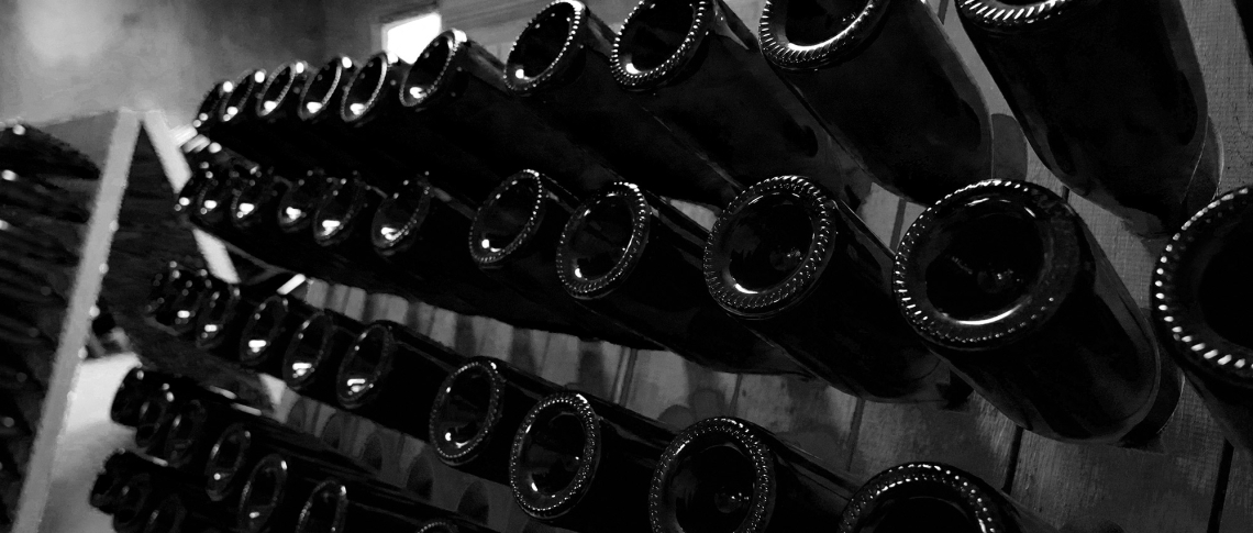 Schwarz-weiß Foto von aufgereihten, kopfüber gelagerten Weinflaschen im Keller.