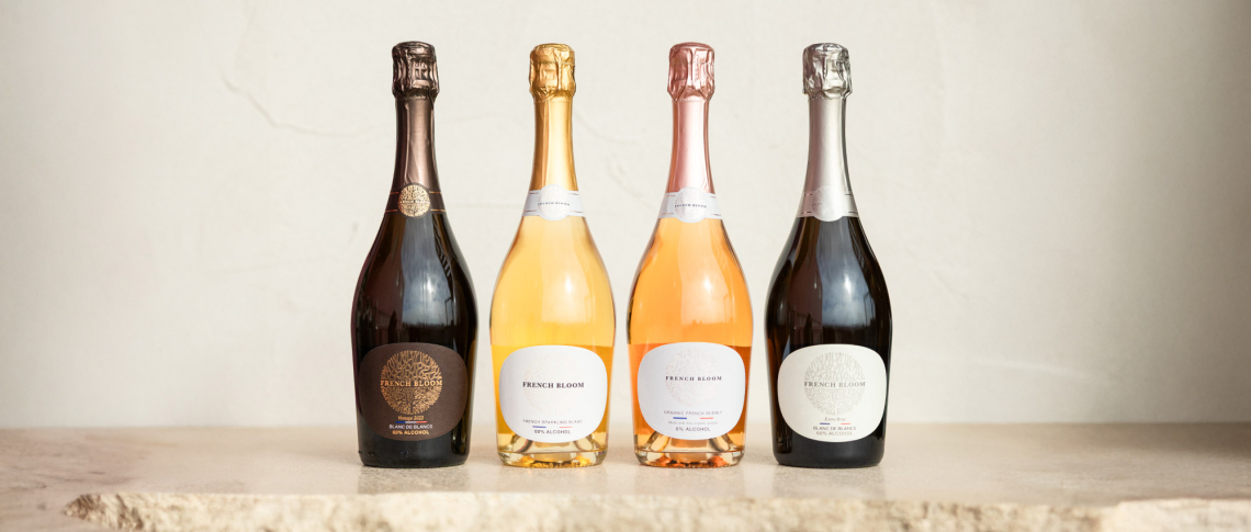 Vier elegante Sektflaschen in verschiedenen Farben auf einer hellen Steinplatte.