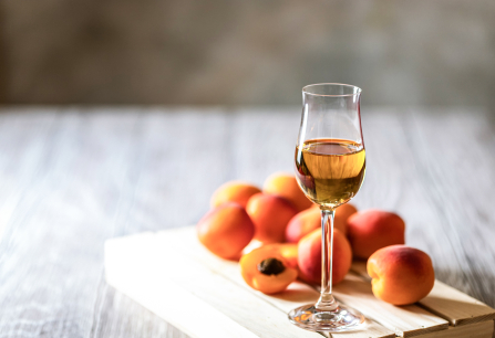 Ein Glas mit bernsteinfarbener Flüssigkeit, umgeben von frischen Aprikosen auf Holz.