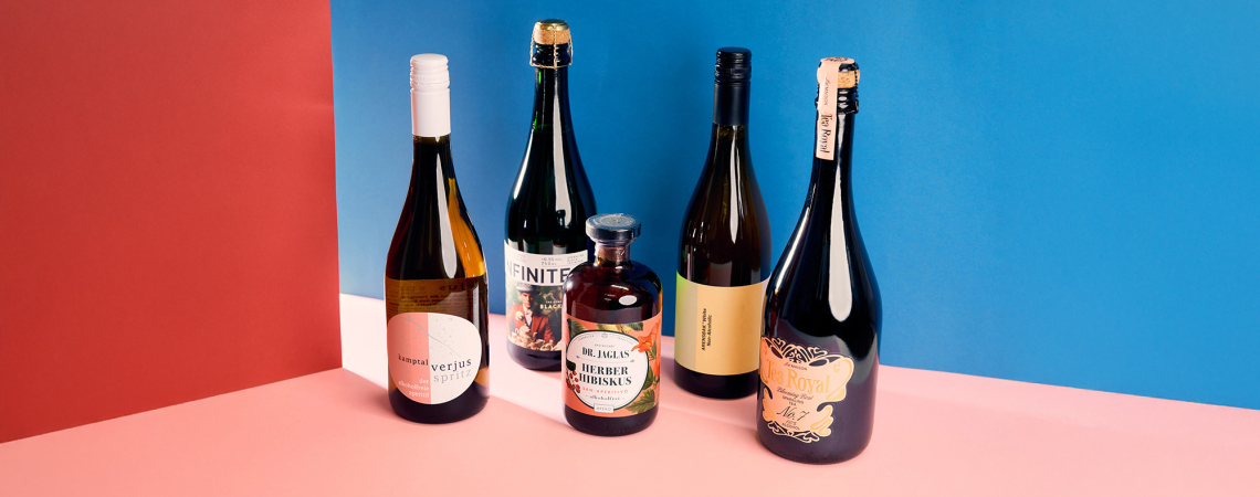 Fünf verschiedene Getränkeflaschen vor rot-blauem Hintergrund auf rosa Boden.