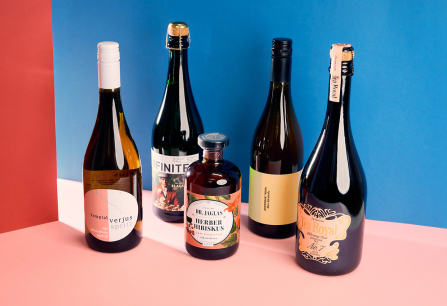 Fünf verschiedene Getränkeflaschen vor rot-blauem Hintergrund auf rosa Boden.