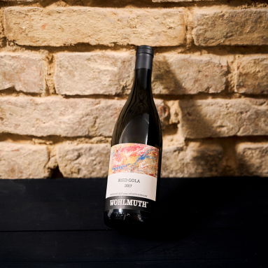 Weinflasche mit künstlerischem Etikett vor rustikaler Ziegelwand.