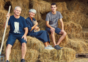 Drei Personen sitzen auf Heuballen vor einem Scheunenhintergrund mit einem Kätzchen.