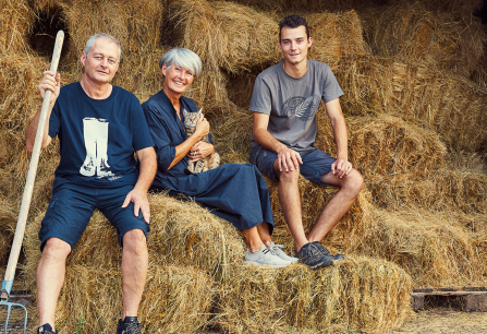 Drei Personen sitzen auf Heuballen vor einem Scheunenhintergrund mit einem Kätzchen.