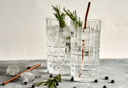 Zwei stilvoll gemusterte Gläser mit Gin Tonic und Rosmarin, Kupferstrohhalm, auf Marmortisch.
