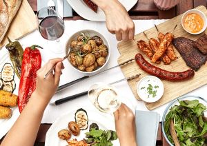 Bunt gedeckter Tisch mit gegrilltem Fleisch, Gemüse, Salat und Brot.