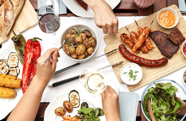 Bunt gedeckter Tisch mit gegrilltem Fleisch, Gemüse, Salat und Brot.