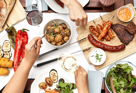 Bunt gedeckter Tisch mit gegrilltem Fleisch, Gemüse, Salat und Brot.