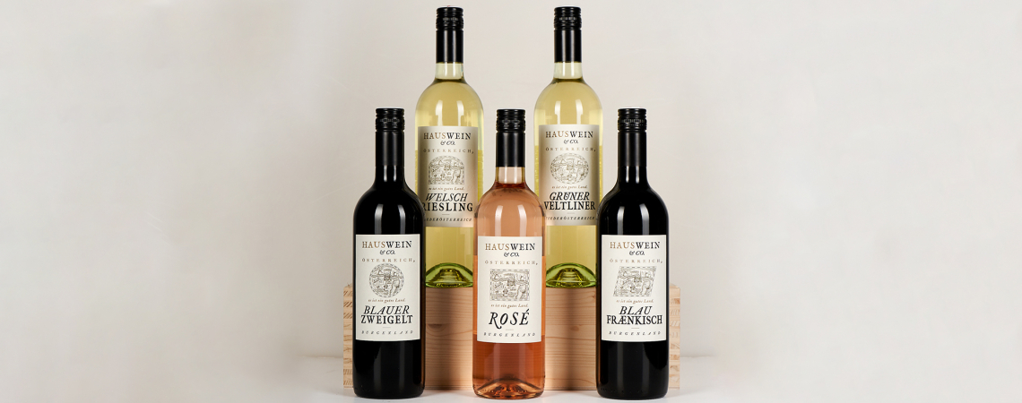 Fünf Weinflaschen in verschiedenen Farben auf Holzbox arrangiert.