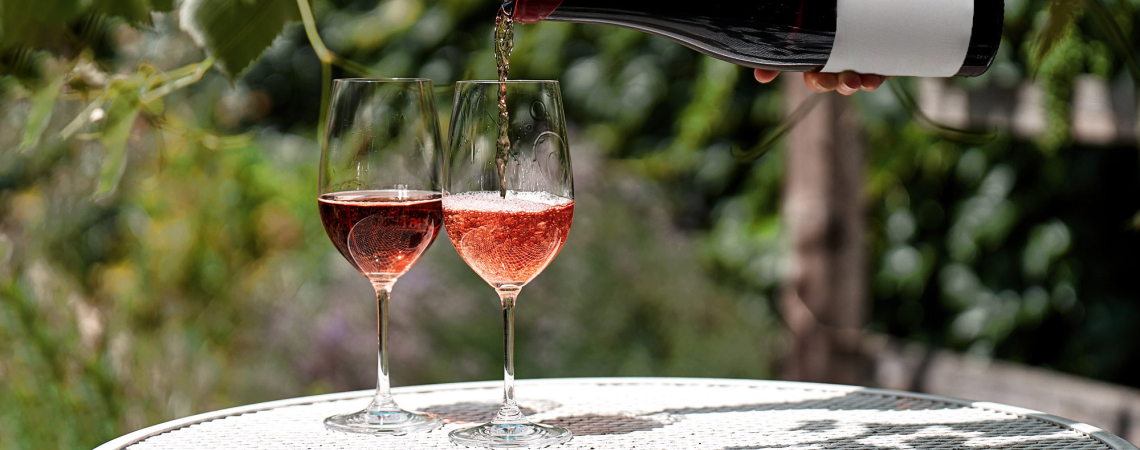 Zwei gefüllte Weingläser auf Tisch im Garten, Flasche im Hintergrund.