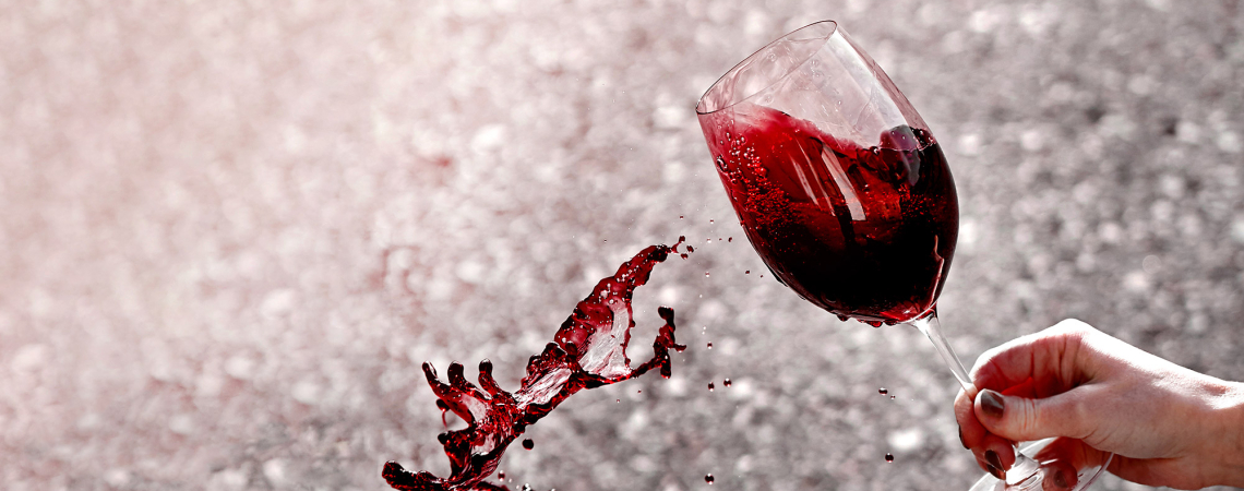 Weinglas mit spritzendem Rotwein vor verschwommenem Hintergrund.