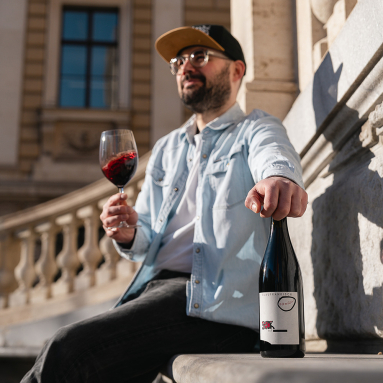 Mann mit Weinglas und Weinflasche, sitzend auf Steintreppe bei Sonnenschein.