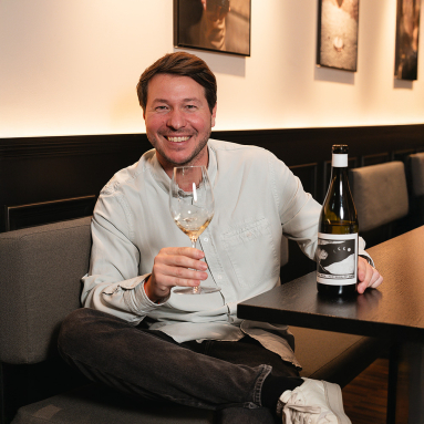 Lächelnder Mann mit Weinglas und Weinflasche in modernem Café.