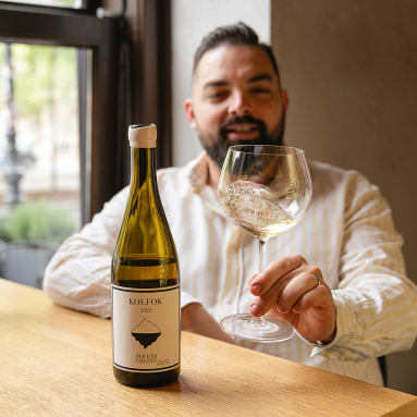 Mann am Tisch mit Weinglas, Weinflasche im Vordergrund, helles Ambiente.