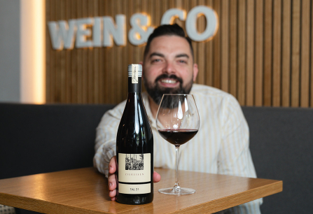 Mann präsentiert Rotweinflasche und gefülltes Weinglas auf Holztisch.