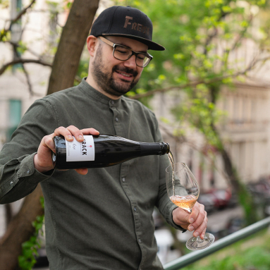 Mann in Olivhemd schenkt Roséwein auf Balkon ein.