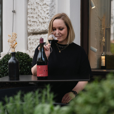 Frau genießt Rotwein auf Terrasse, dekoriert mit schwarzer Vase und Blumen.