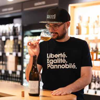 Mann mit Brille und Kappe riecht an Weißweinglas im Geschäft.