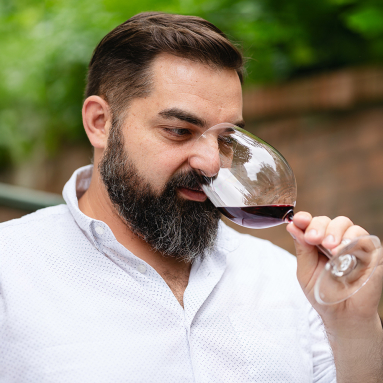 Mann in weißem Hemd riecht an einem Glas Rotwein im Freien.