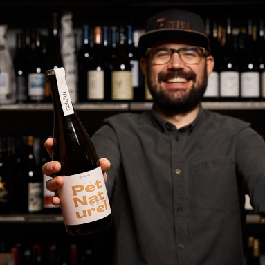 Mann hält Weinflasche vor Regal mit weiteren Flaschen.