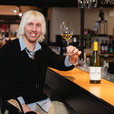 Person in eleganter Umgebung hält ein Glas Weißwein neben einer Weinflasche.