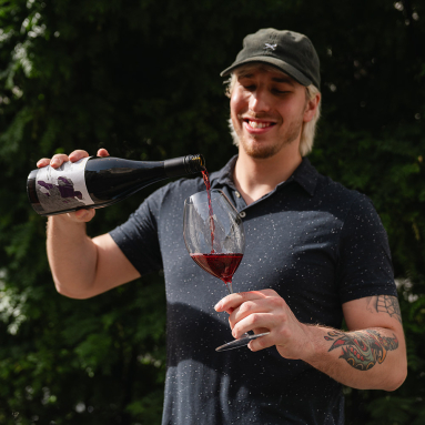 Mann füllt Rotwein aus Flasche in ein Glas, sommerliche Gartenkulisse.