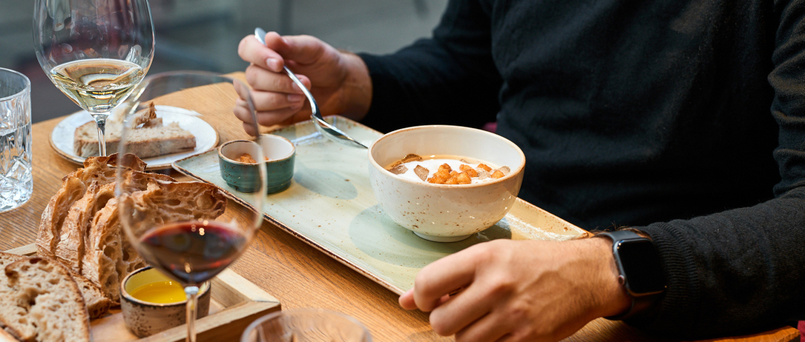 Person isst Suppe an einem gedeckten Tisch mit Brot und Weingläsern.