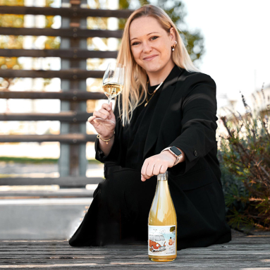 Frau in schwarzem Anzug mit Glas und Weinflasche auf hölzernem Treppenabsatz.