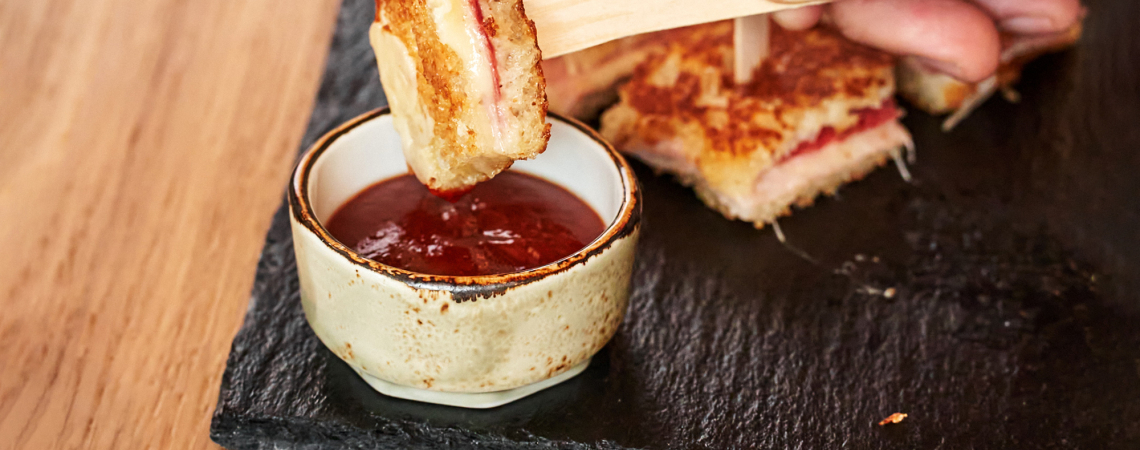 Geröstetes Sandwich in Tomatensoße getaucht, auf Schieferplatte angerichtet.