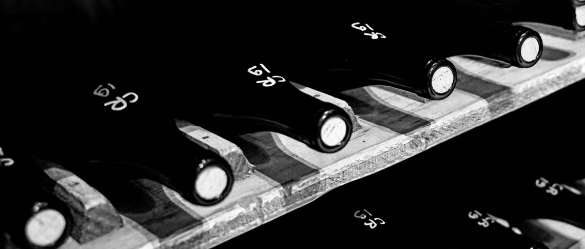 Schwarzweiße Aufnahme von Weinflaschen, liegend in einem rustikalen Regal.