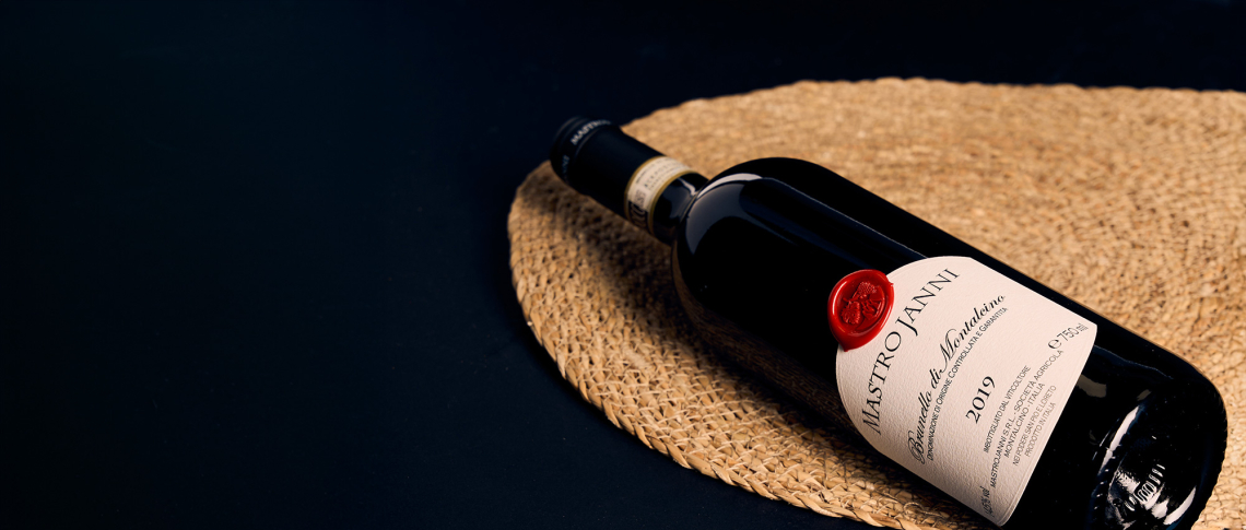 Rotweinflasche mit rotem Siegel auf einem geflochtenen Untersetzer, dunkler Hintergrund.