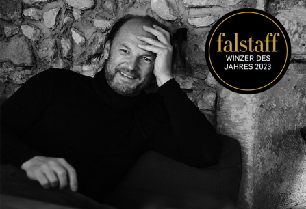 Schwarz-weiß-Bild eines Mannes vor einer Steinmauer, entspannt lächelnd.